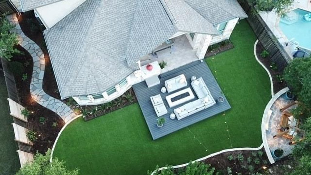 Aerial view of a finished green lawn beside a deck and flagstone patio at a Bee Cave backyard