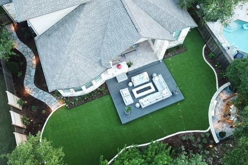 Aerial view of a backyard deck with a flagstone patio and turf under mature live oaks in Bee Cave, near Austin