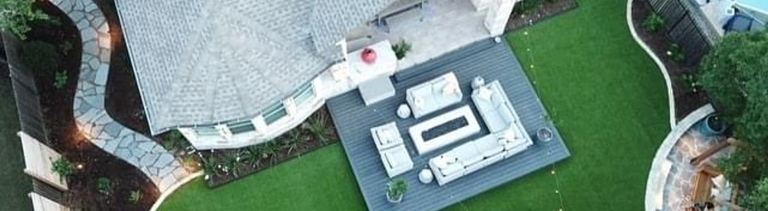 Aerial view of a backyard deck with a flagstone patio and turf under mature live oaks in Bee Cave, near Austin