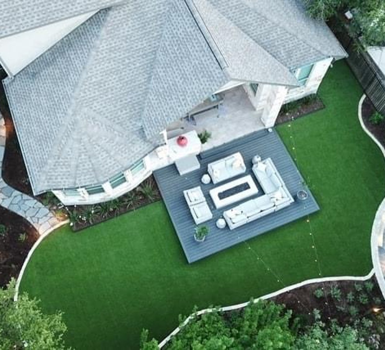 Bee Cave backyard with a composite deck, turf island, and flagstone patio under live oaks