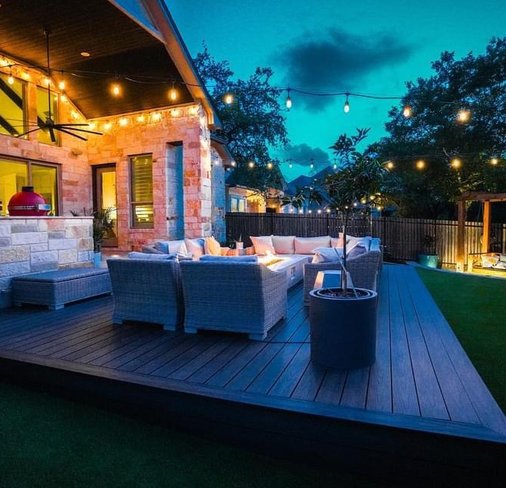 Pergola with string lights over a deck and fire pit at night in a Bee Cave backyard