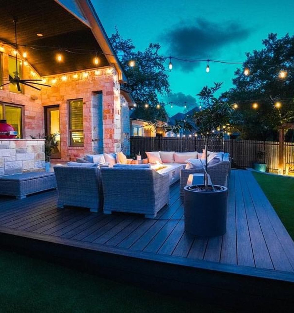 Bee Cave backyard fire pit glowing on a deck under string lights and a pergola at night