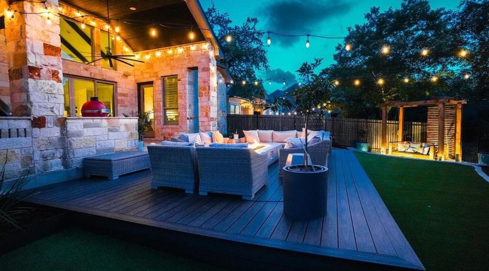 Deck with the linear fire table, pergola, and string lights glowing at night
