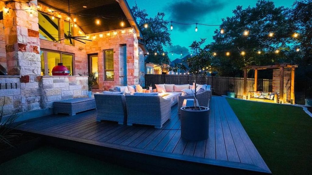 Pergola with string lights over a deck and fire pit lit up at night in a Bee Cave backyard