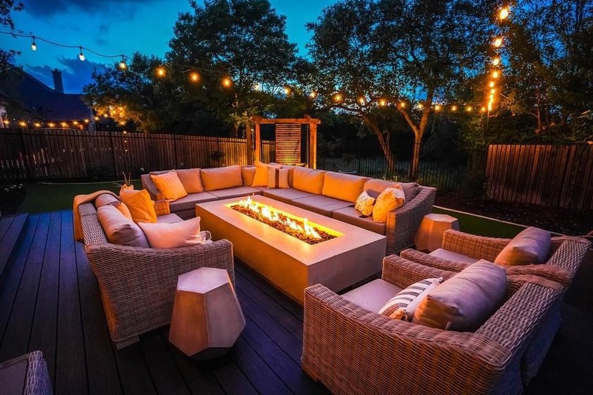Bee Cave backyard at night with a lit fire pit, string lights over the deck, and cedar privacy screens washed with low voltage landscape lighting