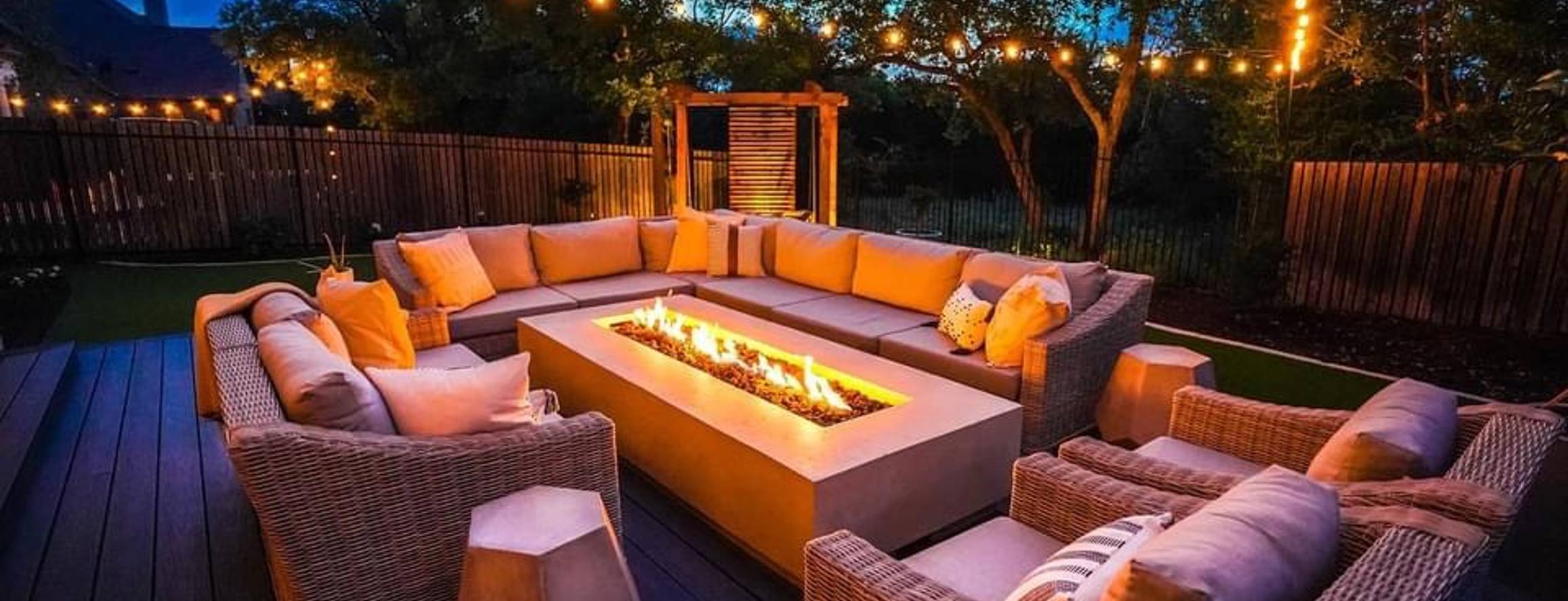 Bee Cave backyard with a deck, firepit, privacy screen, and string lights at night by Thrive Landscape and Design