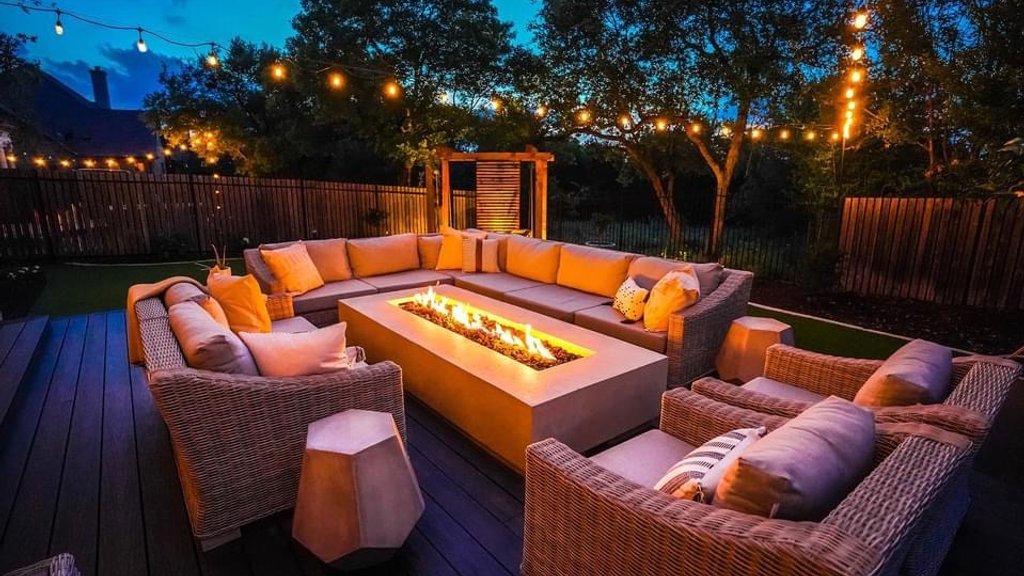 Fire pit lit at night with string lights and a privacy screen on a Bee Cave deck