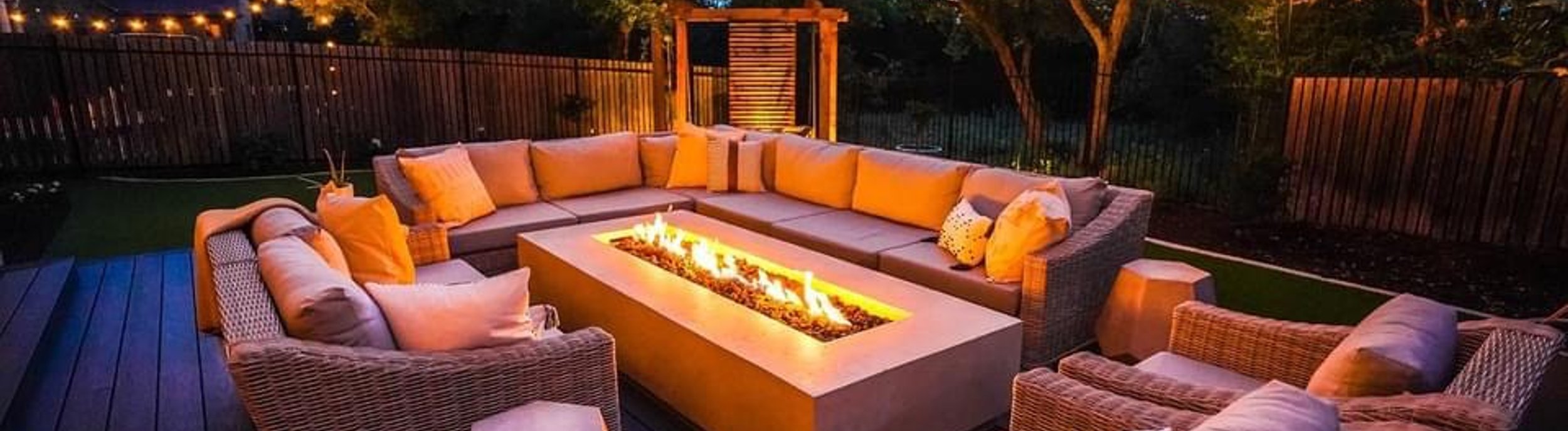 A Bee Cave, TX backyard at night with a deck, fire pit, string lights, and a privacy screen by Thrive Landscape and Design