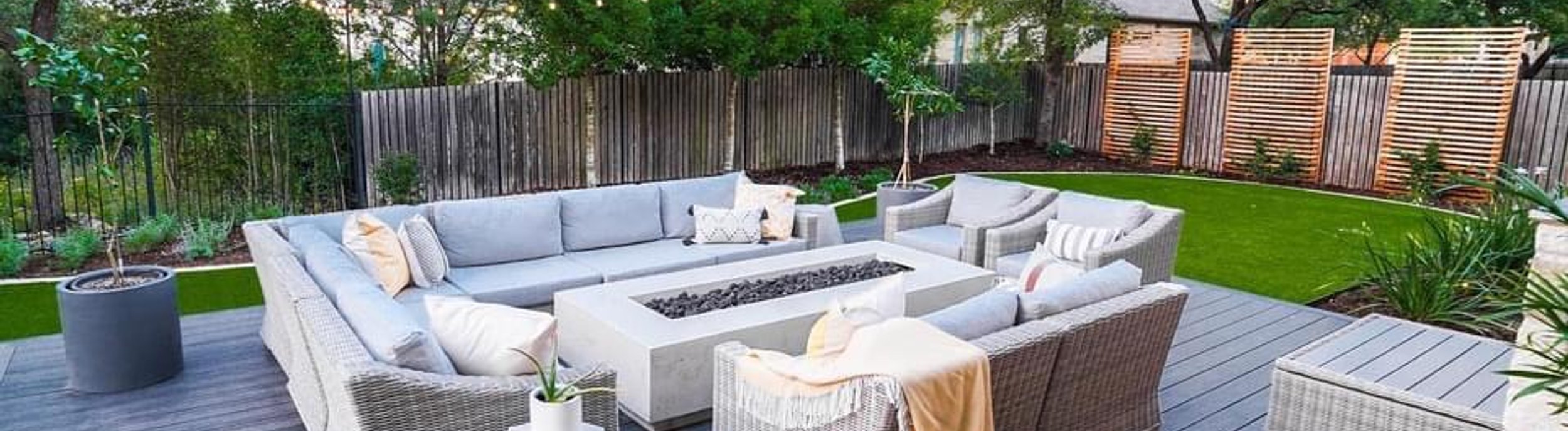 Cedar slat privacy screens rising above a wood fence beside a composite deck and fire table in a Bee Cave backyard