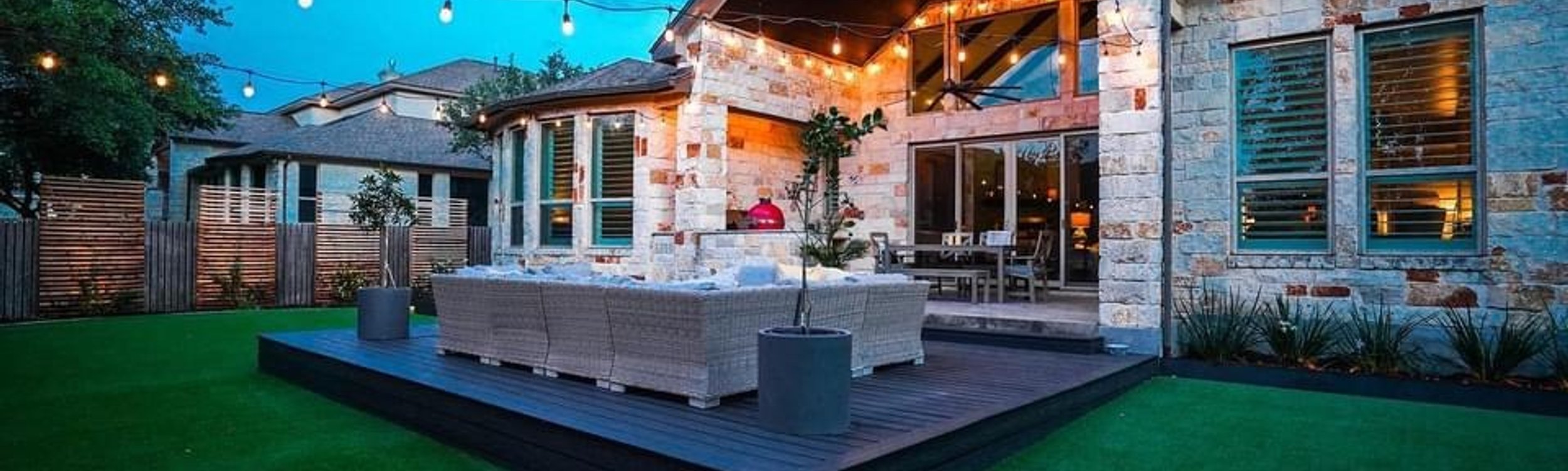 Custom deck with string lights over a turf patio under live oaks in a Bee Cave backyard