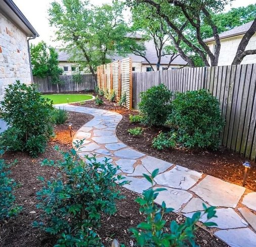 Synthetic turf with a flagstone pathway and planting beds in a Bee Cave backyard
