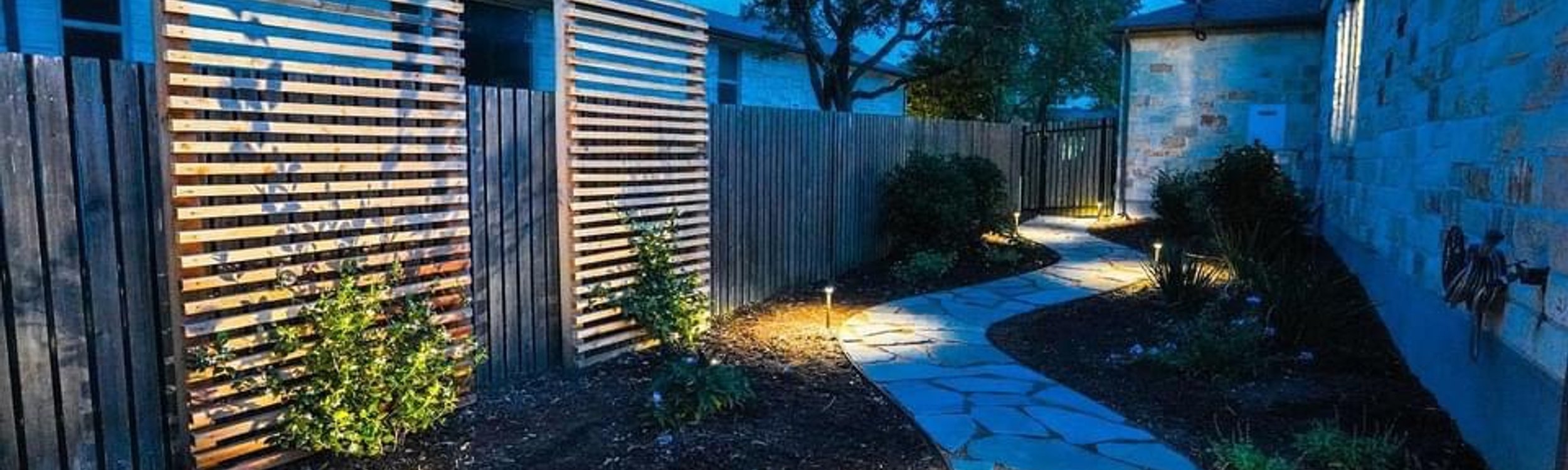 Flagstone pathway lit with low-voltage path lighting and privacy screens in a Bee Cave backyard