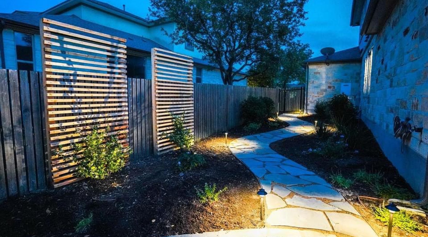 Side-yard flagstone pathway lit by low landscape lighting between privacy screens