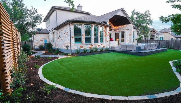 Turf lawn with a stone border, deck, and planting beds at a Bee Cave backyard