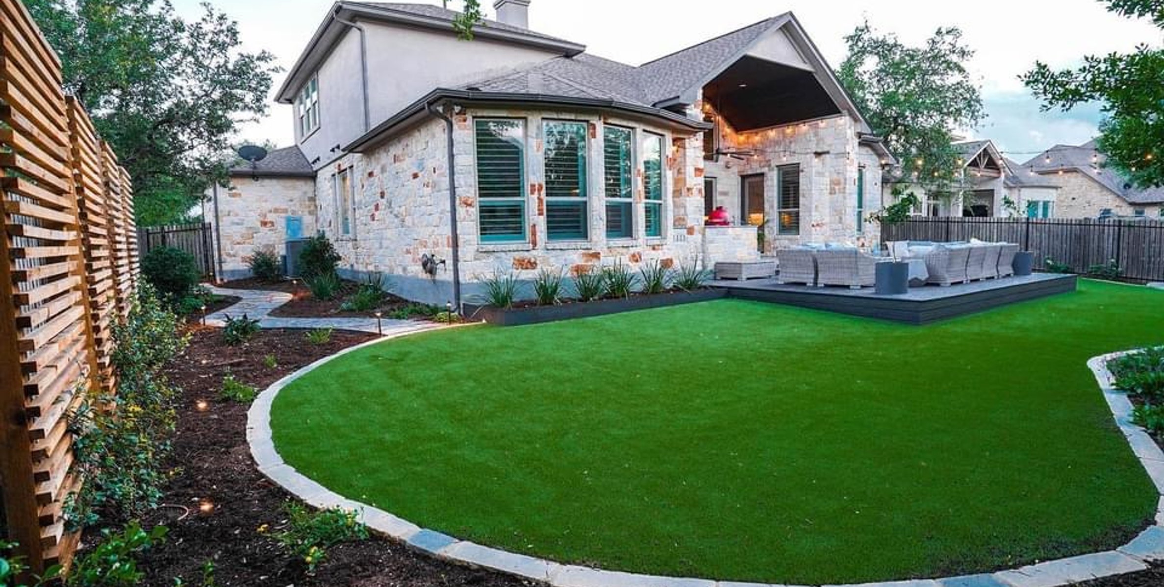 Curved synthetic turf island edged in limestone beside the deck and planting beds