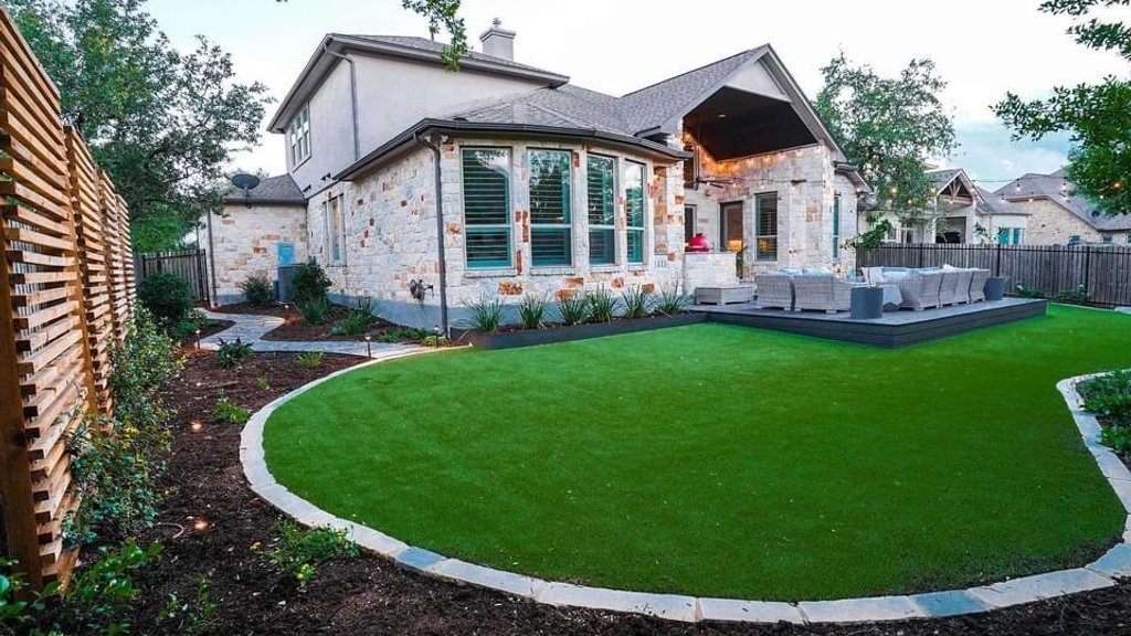 Established turf lawn edged with a stone border beside a deck at a Bee Cave home