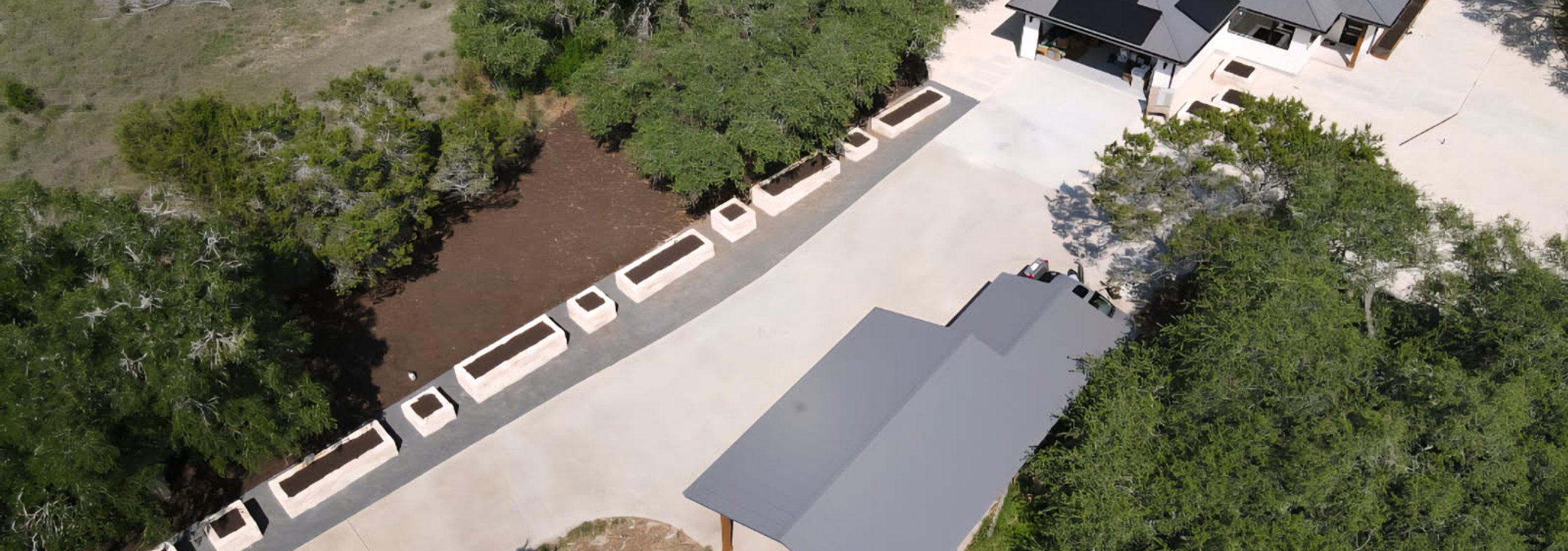 Sweeping concrete driveway lined with uniform raised planting beds