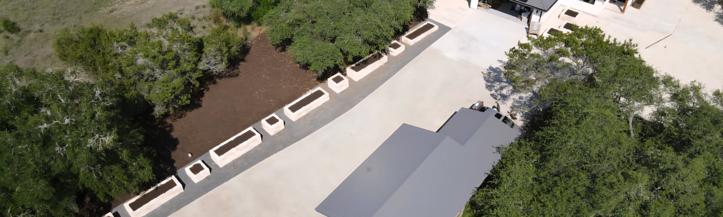 Aerial view of a Driftwood Hill Country lot with drive approach, raised beds, and a planned layout