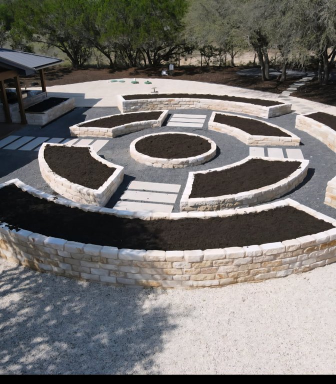 Raised limestone planting beds and a stone paver walkway at a Driftwood garden estate