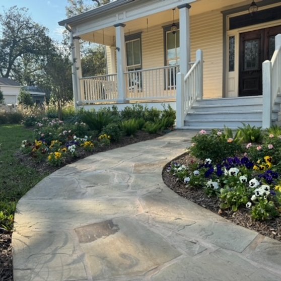 Flagstone walkway beside a healthy lawn and full flower beds at a Central Texas home