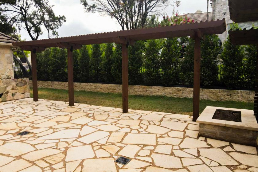 Cedar pergola shading a flagstone patio and fire pit in a Lakeway backyard near Austin