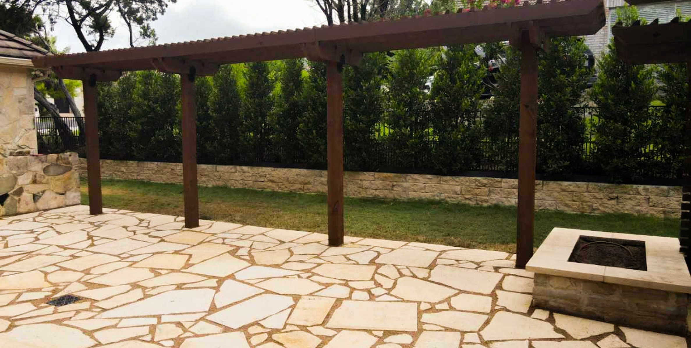 Dark stained pergola over the flagstone patio with a fire pit and string lights