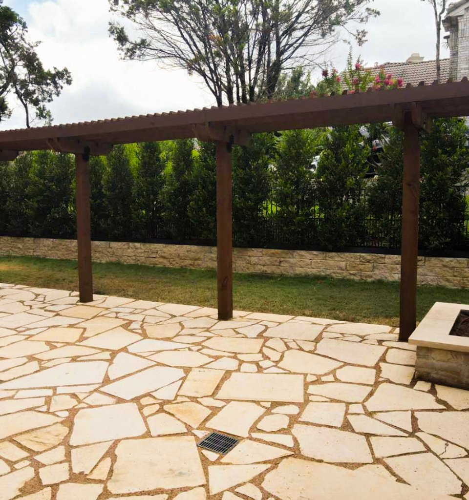 Lakeway flagstone patio with a dark stained pergola and a built-in fire pit