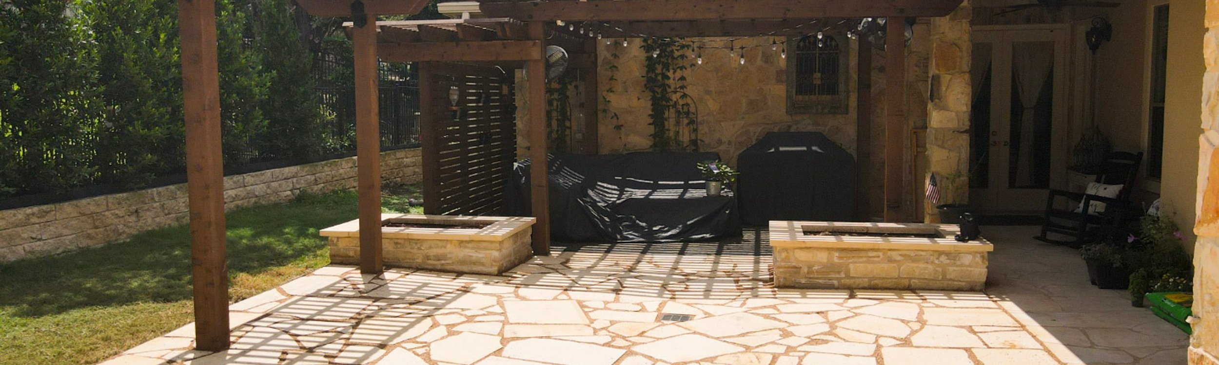 Cedar pergola shading a flagstone patio with stacked-stone planters at a Lakeway home near Austin