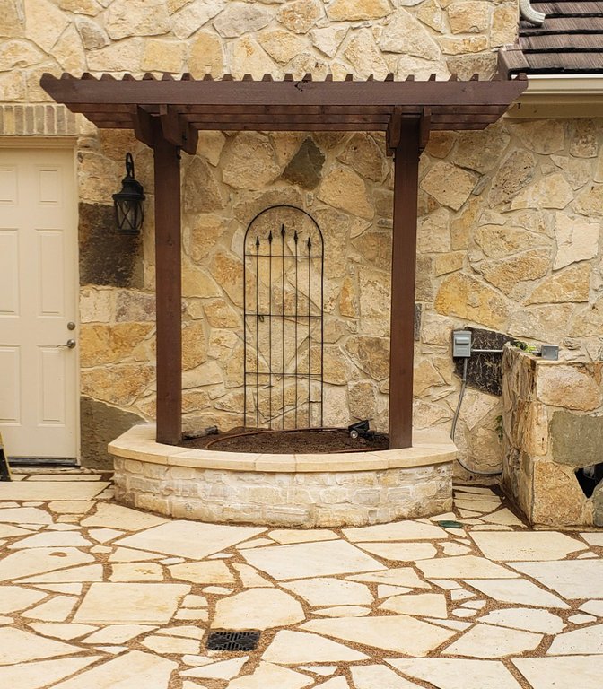 Cedar trellis with an iron gate over flagstone and a stone planter at a Lakeway property