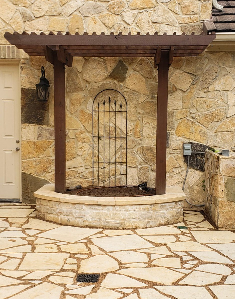 Curved limestone raised bed with a small pergola framing an arched iron gate