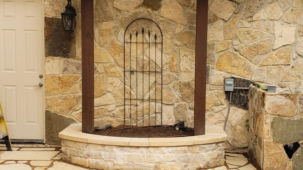 Trellis, iron gate, and stone planter framing a flagstone area at a Lakeway home
