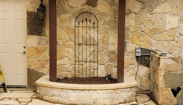 Cedar trellis structure with an iron gate over a flagstone path and stone planter in Lakeway