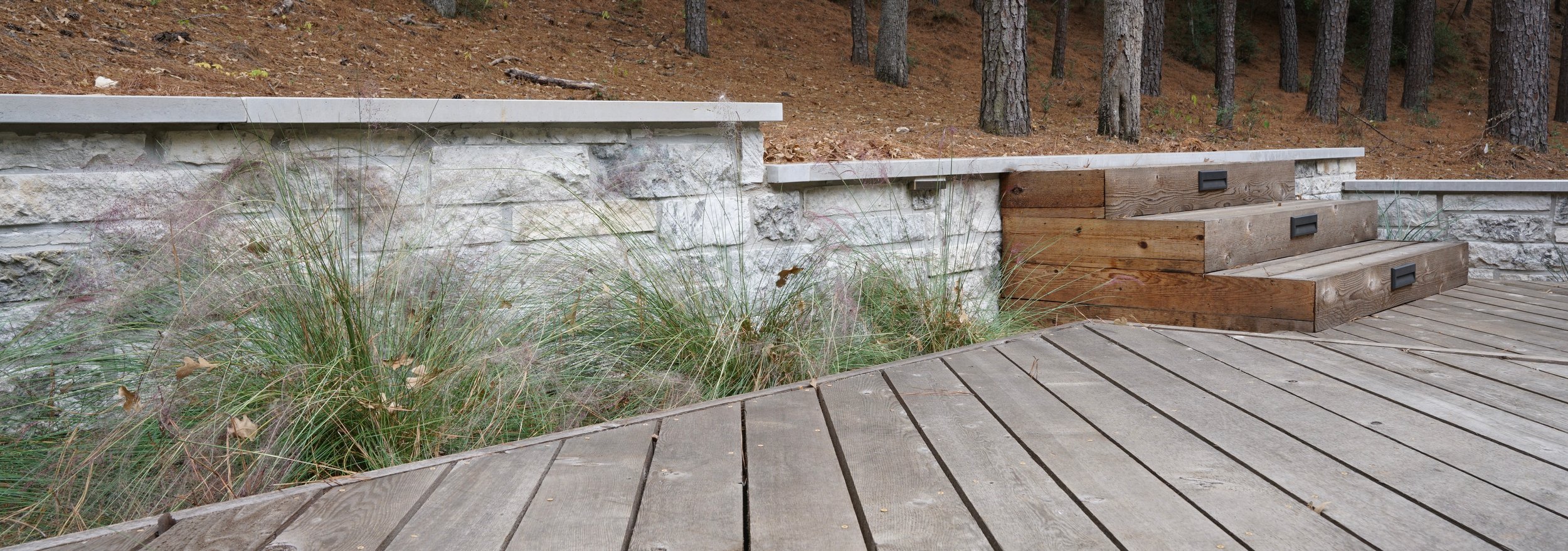 Weathered wood deck meeting limestone retaining walls and timber steps with recessed lighting