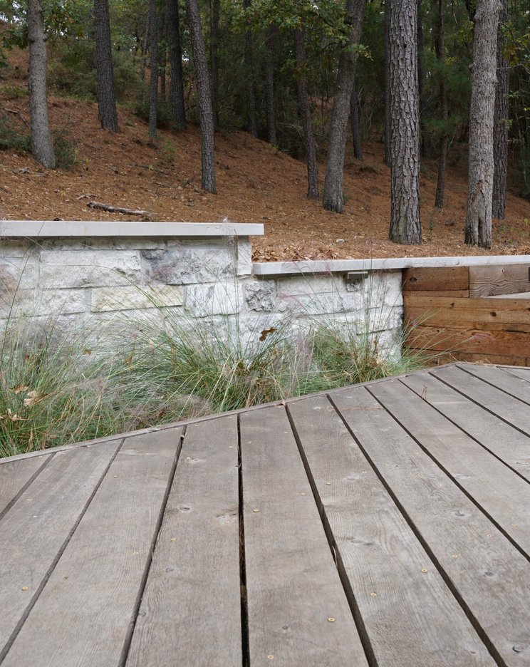 Sloped Lost-Pines backyard with a custom deck, retaining wall, and steps
