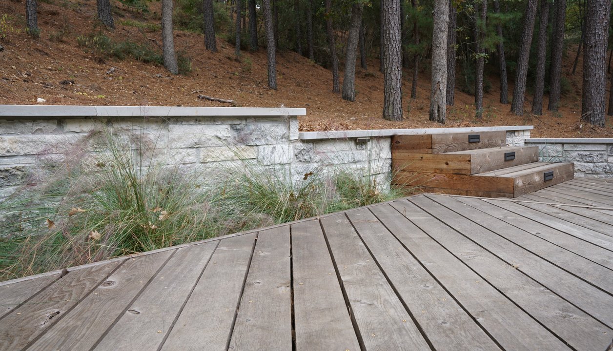 Multi-level deck with a stone retaining wall and steps on a Lost Pines lot