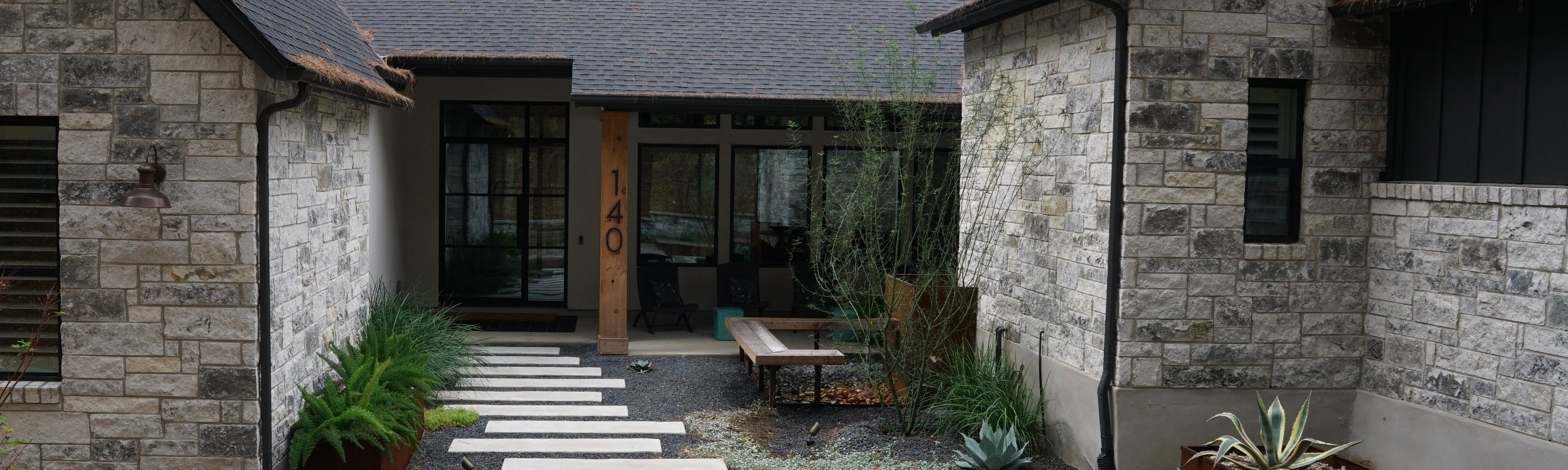 Lost Pines property with a paver patio, deck, raised planters, and xeriscape plantings from a phased landscape plan