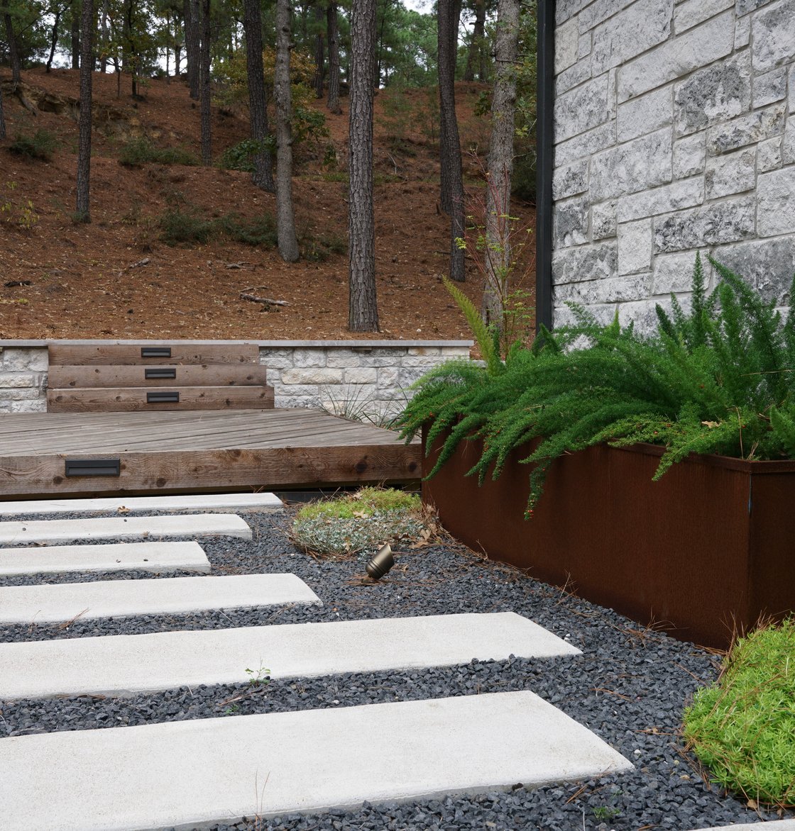 Bastrop Lost Pines courtyard with pavers, gravel, steel planters, and a deck