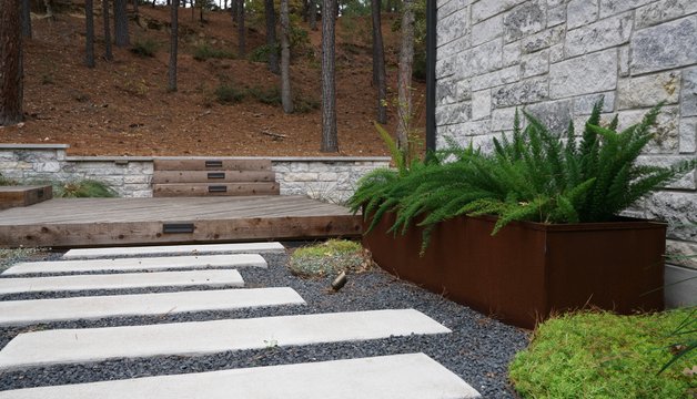 Bastrop Lost-Pines hardscape with pavers, gravel, planters, and a deck integrated into the grade