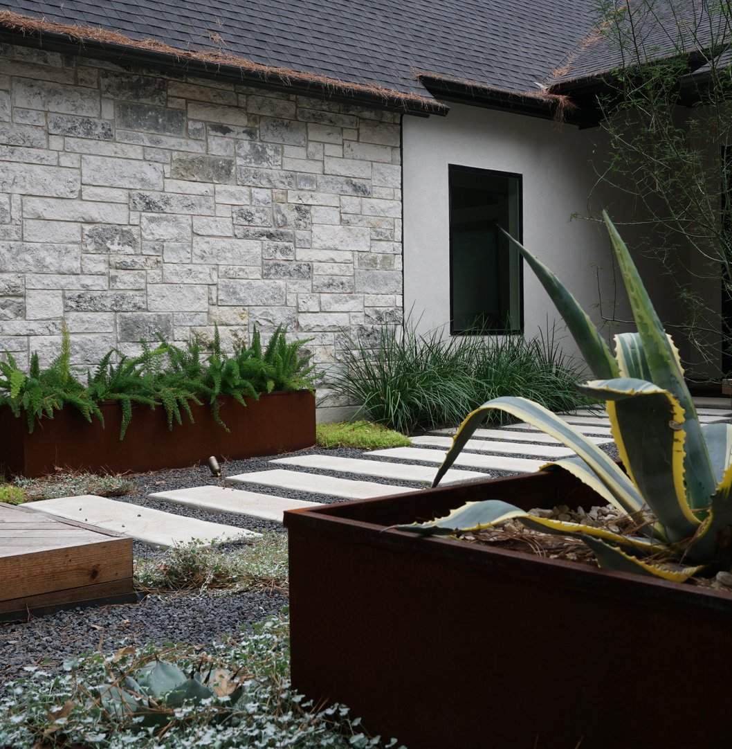 Lost Pines courtyard in Bastrop with paver patio, steel planters, and a low-water xeriscape design