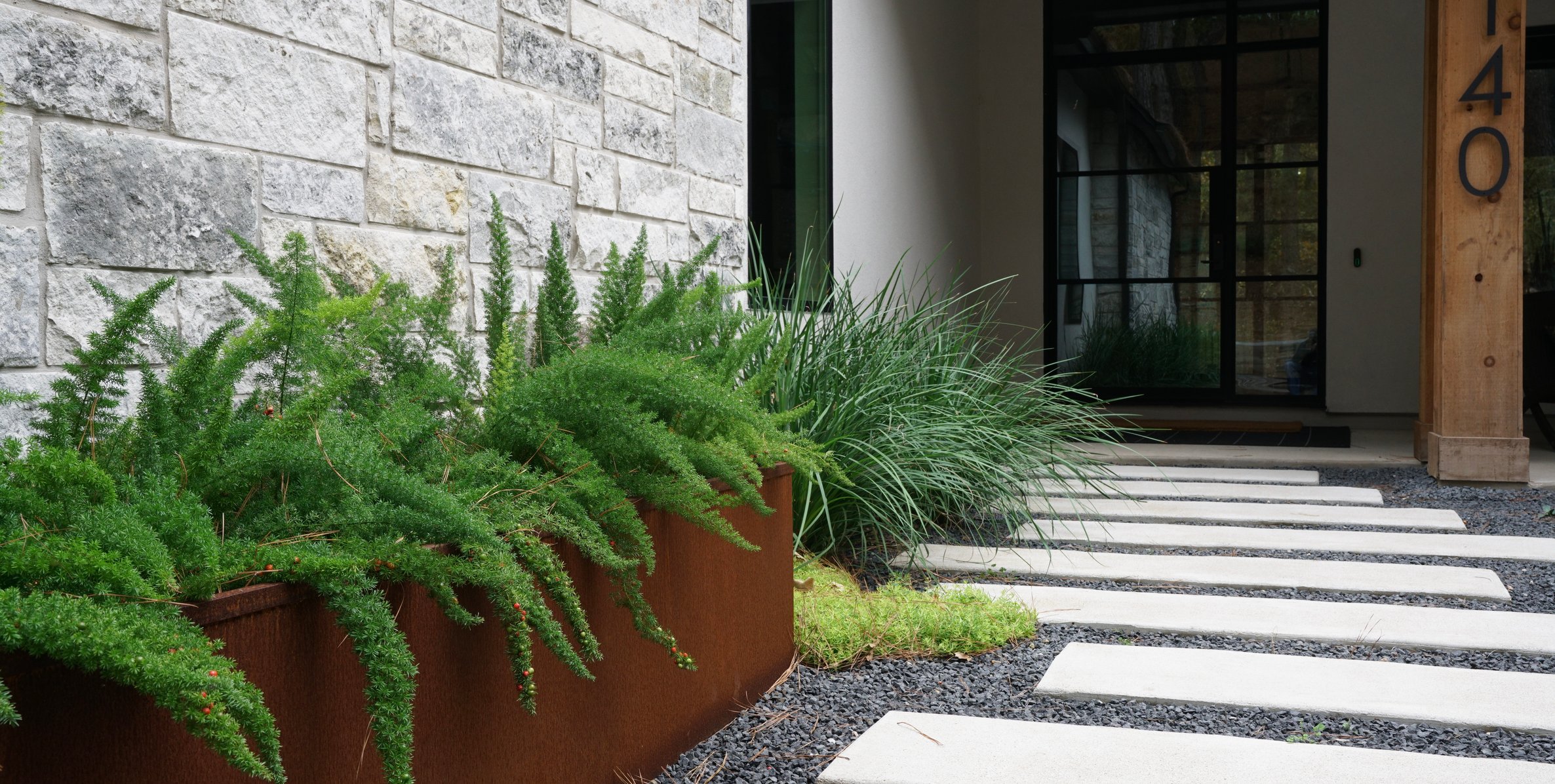 Linear cream paver walkway set in black decomposed granite with Corten steel planters