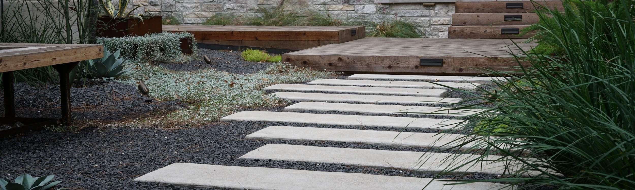 Paver walkway with a retaining wall and deck at a Lost Pines landscape near Austin