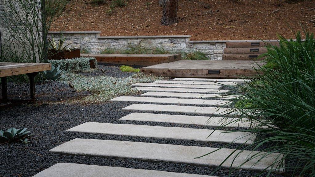 Sloped Lost-Pines lot with a paver walkway, retaining wall, and tiered deck