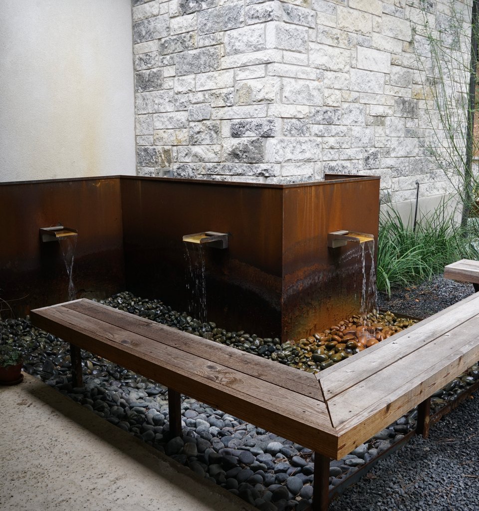 Bastrop Lost-Pines courtyard with a corten water feature and a built-in timber bench