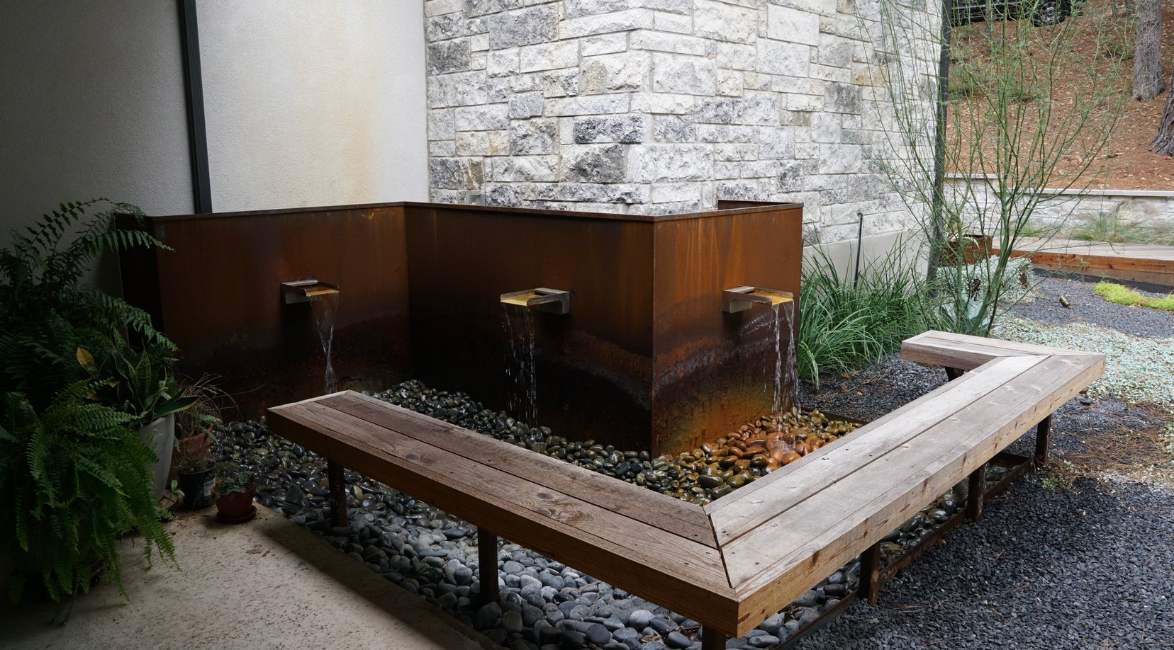 Reclaimed wood bench wrapping the Corten water feature over a river rock catch basin