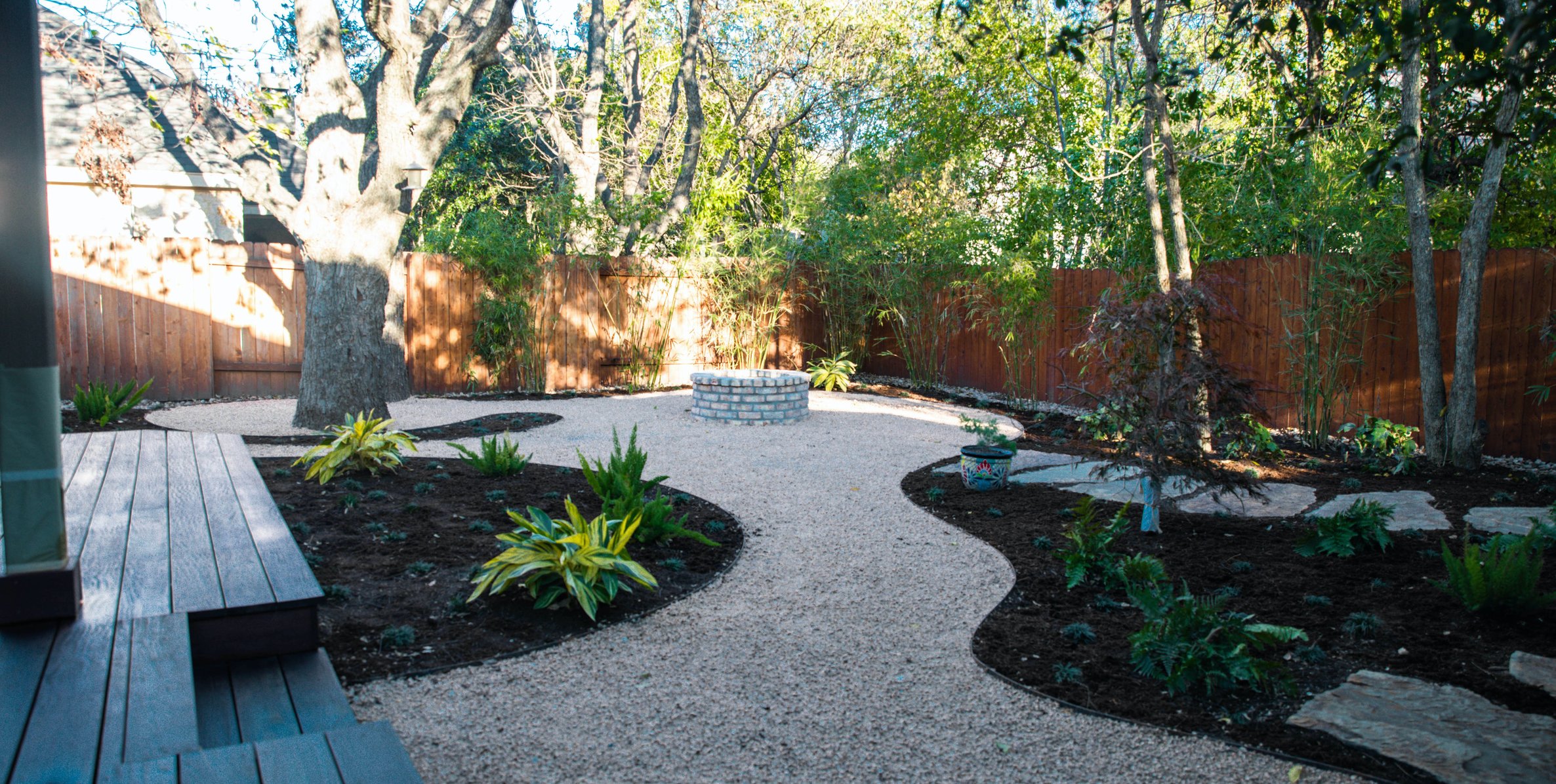 Deck and brick fire pit set among decomposed granite paths and shade planting beds