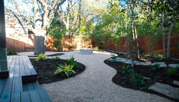 Low wood deck set into a shaded River Place backyard with a fire pit and planting beds