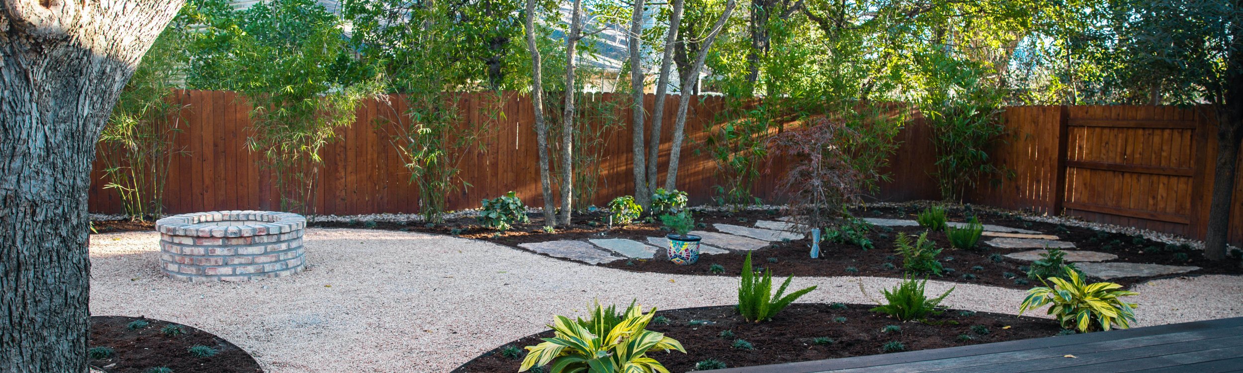 Outdoor living space with a deck, fire pit, decomposed granite paths, and planting beds in a Riverplace, Austin garden