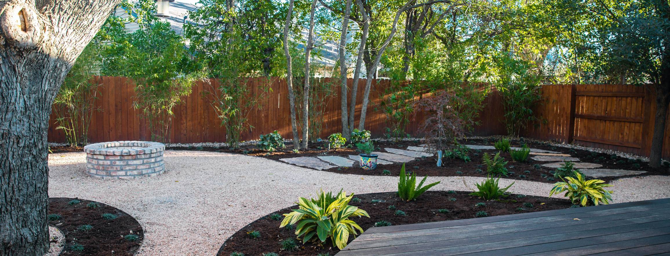 River Place shaded garden with a deck, firepit, decomposed granite, and planting beds by Thrive Landscape and Design