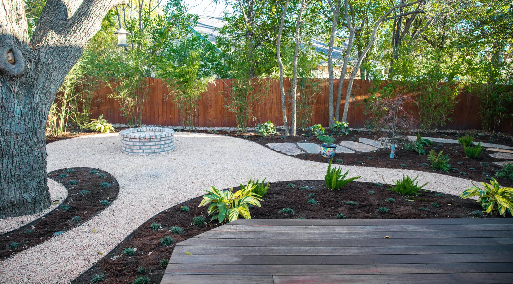 Decomposed granite curves around steel-edged planting beds beside the deck
