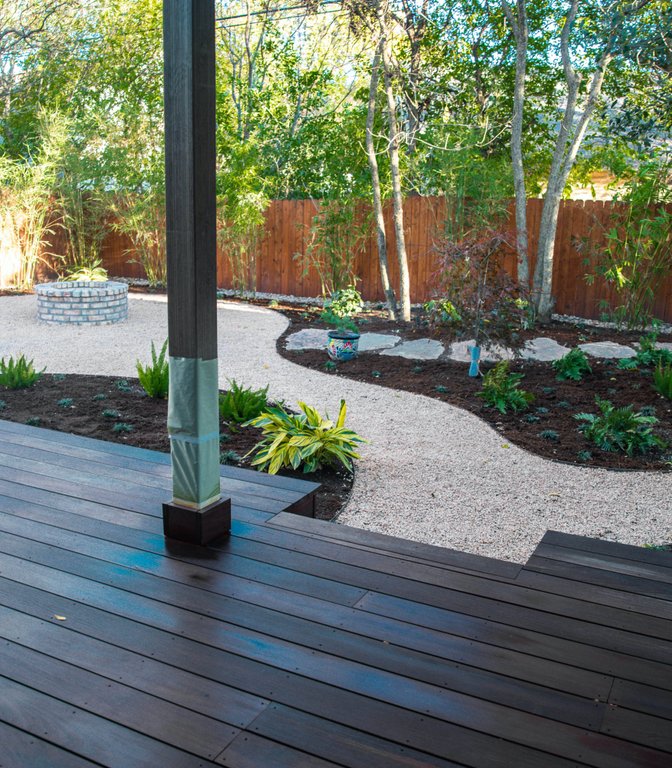 Same River Place yard after renovation with a deck, fire pit, flagstone, and fresh planting beds